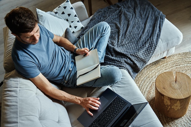 Above view of man sitting on sofa and using laptop freelancer working at home workplace remote work