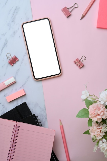 Above view of mock up smartphone and office supplies on pink and marble background.