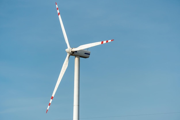 View of a modern windmill against a blue sky The white blades of the wind turbine close up Renewable energy source Production of cheap and safe electricity