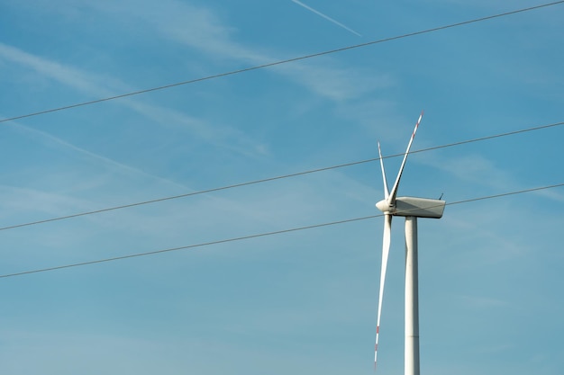 View of a modern windmill against a blue sky The white blades of the wind turbine close up Renewable energy source Production of cheap and safe electricity