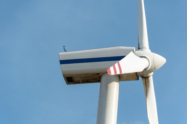 View of a modern windmill against a blue sky The white blades of the wind turbine close up Renewable energy source Production of cheap and safe electricity