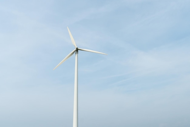 View of a modern windmill against a blue sky The white blades of the wind turbine close up Renewable energy source Production of cheap and safe electricity