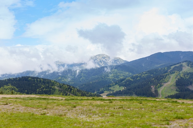 View of mountain with rocky foreground, green meadows, tourist path in distance, beautiful nature, amazing landscape