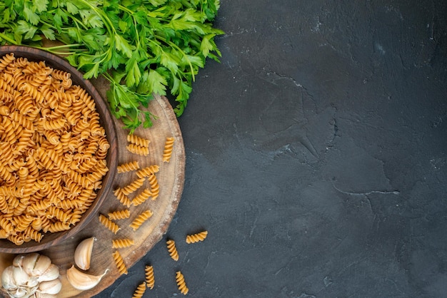 Above view of raw pastas inside and outside brown pot green bundle on dark blue color background