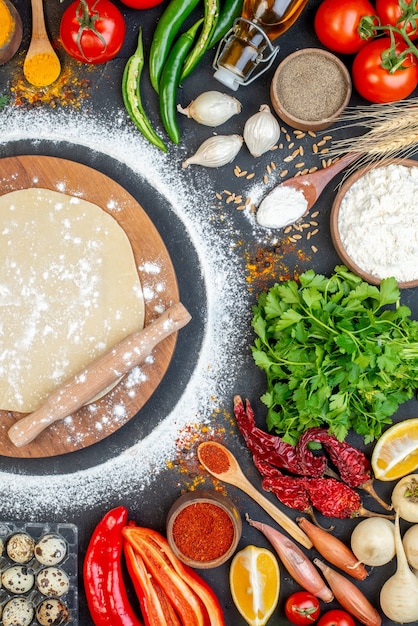 Above view of rolling pin over the circle dough on wooden board and set of foods on black background