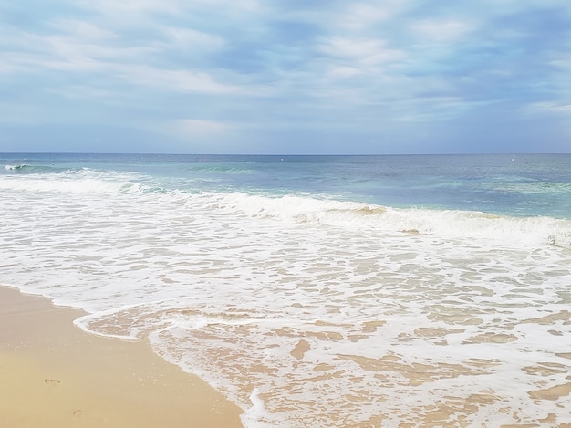 View of the sandy beach, blue sea, foam and gloomy sky in the morning at sunrise.