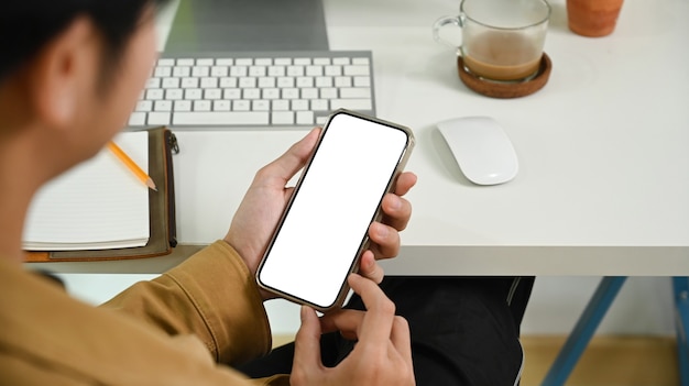 View over shoulder of businessman using smart phone at office desk.