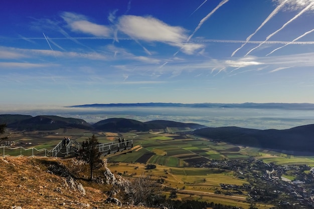 View to a skywalk and wide green valley with fog and blue sky