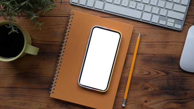 Above view smart phone with blank display notebook and coffee cup on wooden table