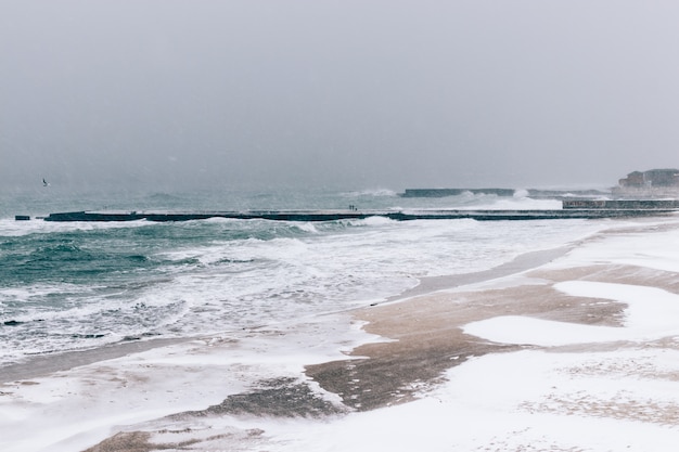 View of snow-covered pier and the sea during a snowfall in winter