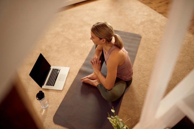 Above view of sportswoman practicing Yoga while using laptop at home