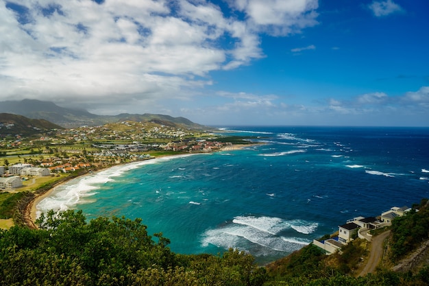 A view over St. Kitts Island with residential area and beach on the foreground and lush green hills