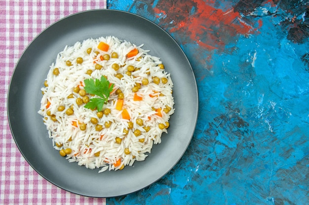 Above view of tasty rice meal for dinner with pisum carrot on purple stripped towel on blue table