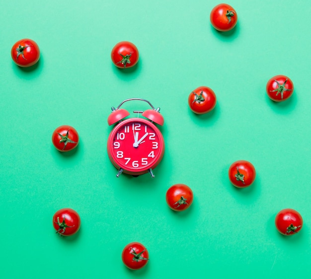 Above view at tomatoes and alarm clock on green background