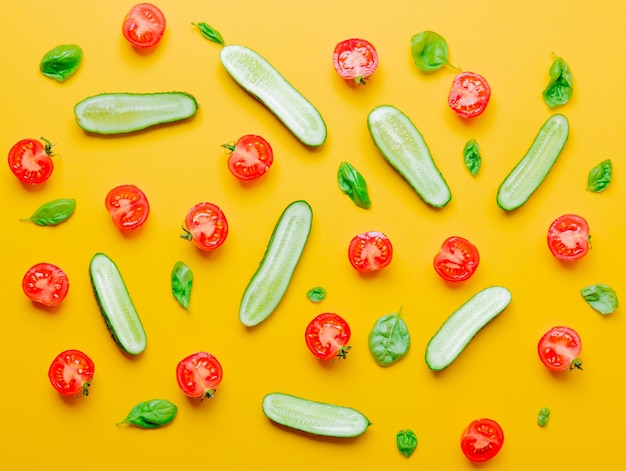 Above view at tomatoes, cucumbers and basil on yellow background