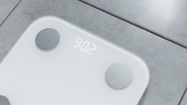 Photo above view of white electric scales displaying weight kilograms grey tile floor closeup