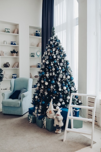 View over white modern room decorated for Christmas holidays. Decorated and illuminated Christmas tree, fireplace with fir branch, candles and handmade paper stars in fireplace.