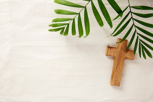 Above view wooden cross and leaves on sand