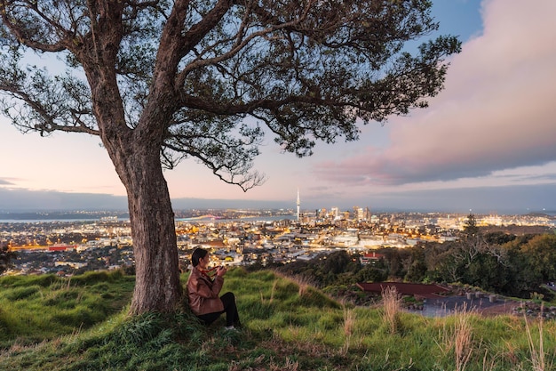 Viewpoint of Mount Eden with female tourist relaxing and sky tower among illuminated city at Auckland New Zealand