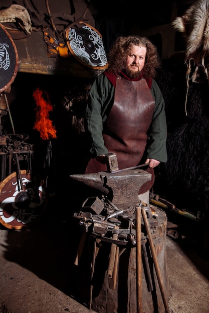 Viking forges weapons and swords in the smithy. A man in a warrior's clothes is in the smithy.