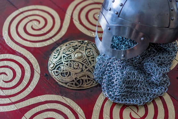 Viking helmet with chain mail on a red shield with golden shapes of sun weapons for war