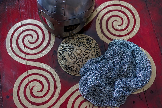 Viking helmet with chain mail on a red shield with golden shapes of sun weapons for war