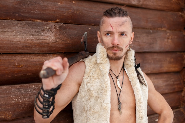 Viking Warrior with an Ax in a Vest of a Skin near a Wooden Wall