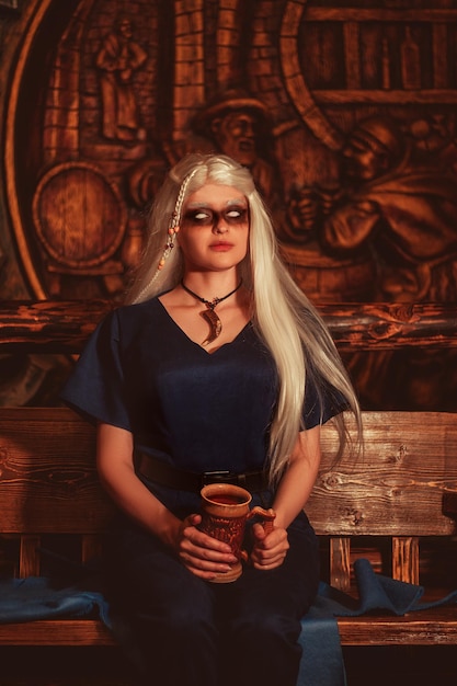 Viking woman with a mug in traditional warrior clothes inside a pub