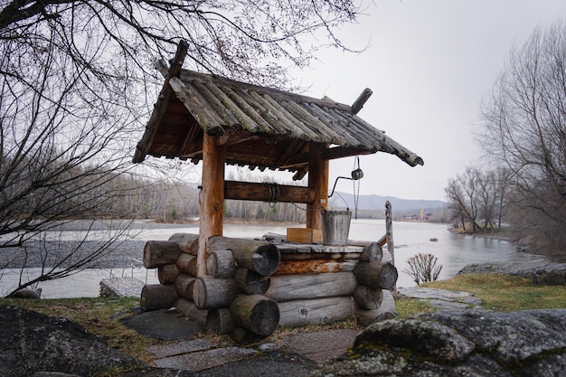 Village well under the roof with a metal chain on a cloudy autumn against the background of the rive