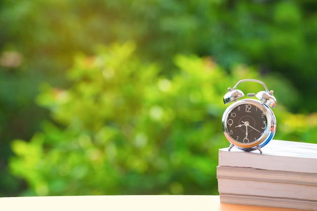 Vintage alarm clock on rustic book on green burred background.