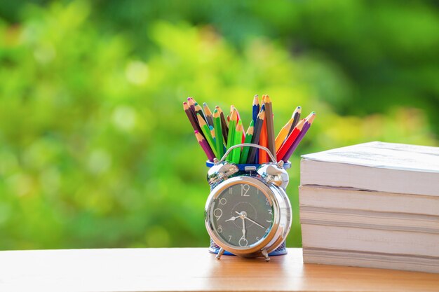 Vintage alarm clock  with color pencil and rustic book on green burred background.