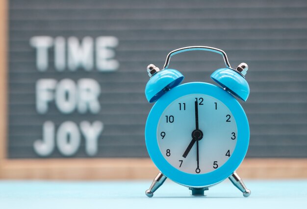 Vintage blue alarm clock at the background of the inscription a time for joy in English