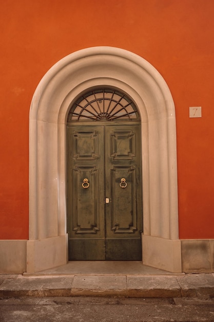 Vintage brown green wooden door with orange wall in Italy