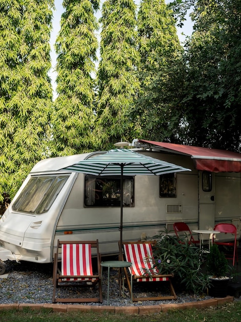 Vintage caravan car parking in garden decoration with empty seats and table on big tree background vertical style Relax camping and sleep in the motorhome trailer Family vacation travel concept