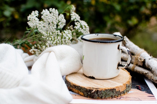 Vintage cup with coffee stands on a wooden stand sweater and flowers in the background