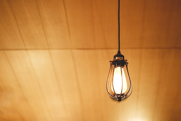 Vintage Edison light bulb hanging over against wooden background in cafe.