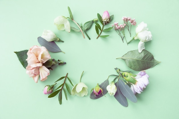 Vintage floral frame with rosebuds, delicate white flowers, branches, leaves and petals on a green background. Flat layout, top view