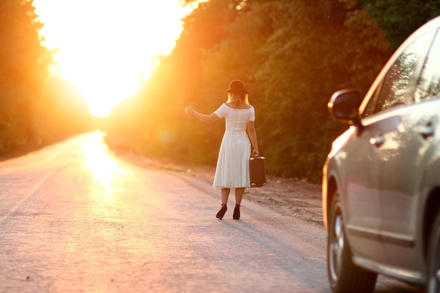 Vintage girl with hat with a suitcase hitchhiking