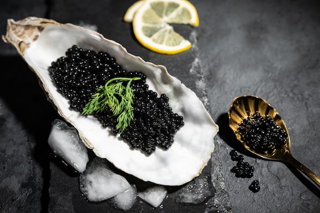 Vintage golden spoon with black sturgeon caviar and oyster on black slate stone table. Copy space