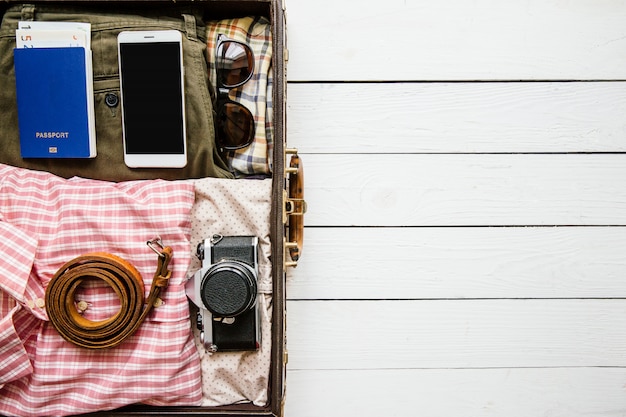 Vintage hipster clothes and accessories packed in suitcase for travel on white wooden table with copy space