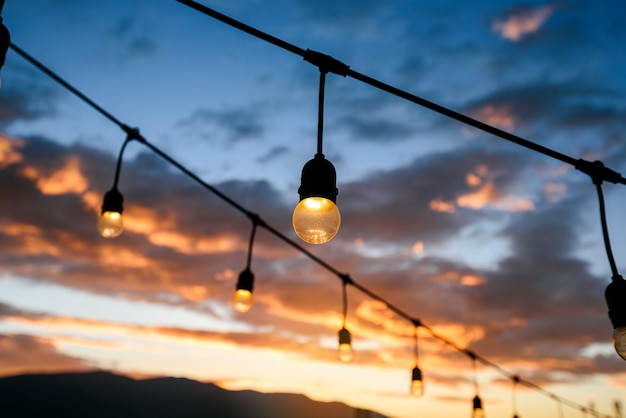 Vintage light bulbs on string wire against sunset sky decor in outdoors wedding event party