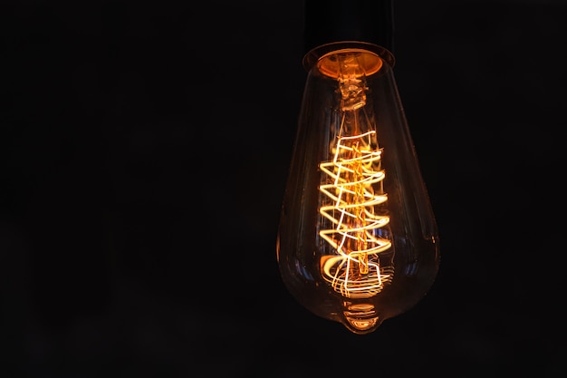 Vintage lightbulb on dark surface with bright yellow shining wire.