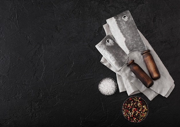 Vintage meat knife hatchets on kitchen towel and black stone table background. Butcher utensils.