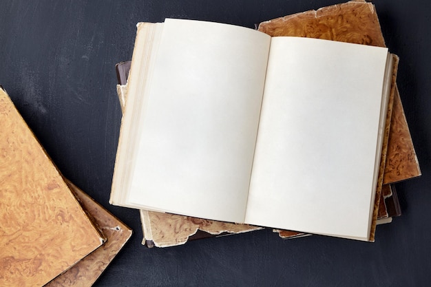 Vintage notepad book with blank pages lies on a stack of shabby books on a black concrete table