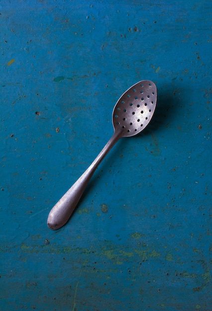 Photo vintage old aluminum spoon skimmer with the holes in the dirty blue background, close-up, top view