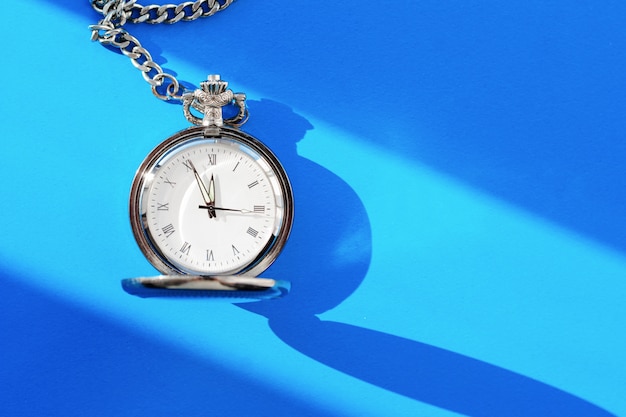 A vintage pocket watch shows twelve hours on a blue background.