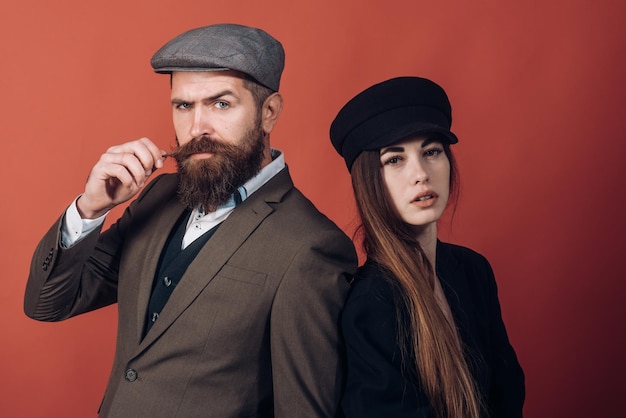 Photo vintage retro couple on red wall old style hat on bearded man and black fashion cap on beauty woman