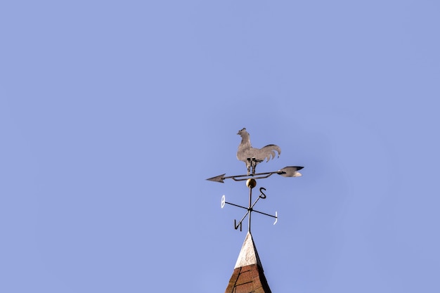 Vintage rooster weathervane, cardinal points north, south, east and west, with blue sky in the surface