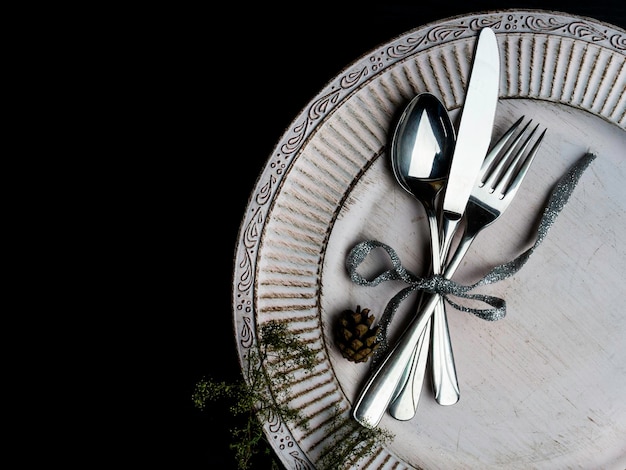 Vintage or rustic christmas table setting Elegant white plate cutlery and natural pine tree branch on wooden surface