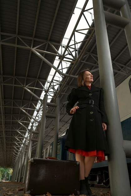 Vintage style young woman with leather suitcase stands on train station Retro style Vertical frame